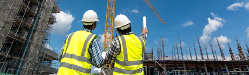 Deux ouvriers échangent sur un chantier avec des échafaudages et une grue au fond afin d'évoquer la reprise d'activité du BTP après la crise sanitaire et la mise en place des gestes barrières