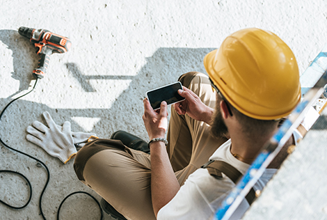 2 Un ouvrier avec son casque sur un chantier utilise son téléphone portable pour aller voir son espace client depuis l'application mobile MBTP