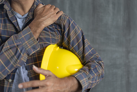 2 Ouvrier qui tient son casque dans ses mains et qui appui sur son épaule pour évoquer une douleur de TMS